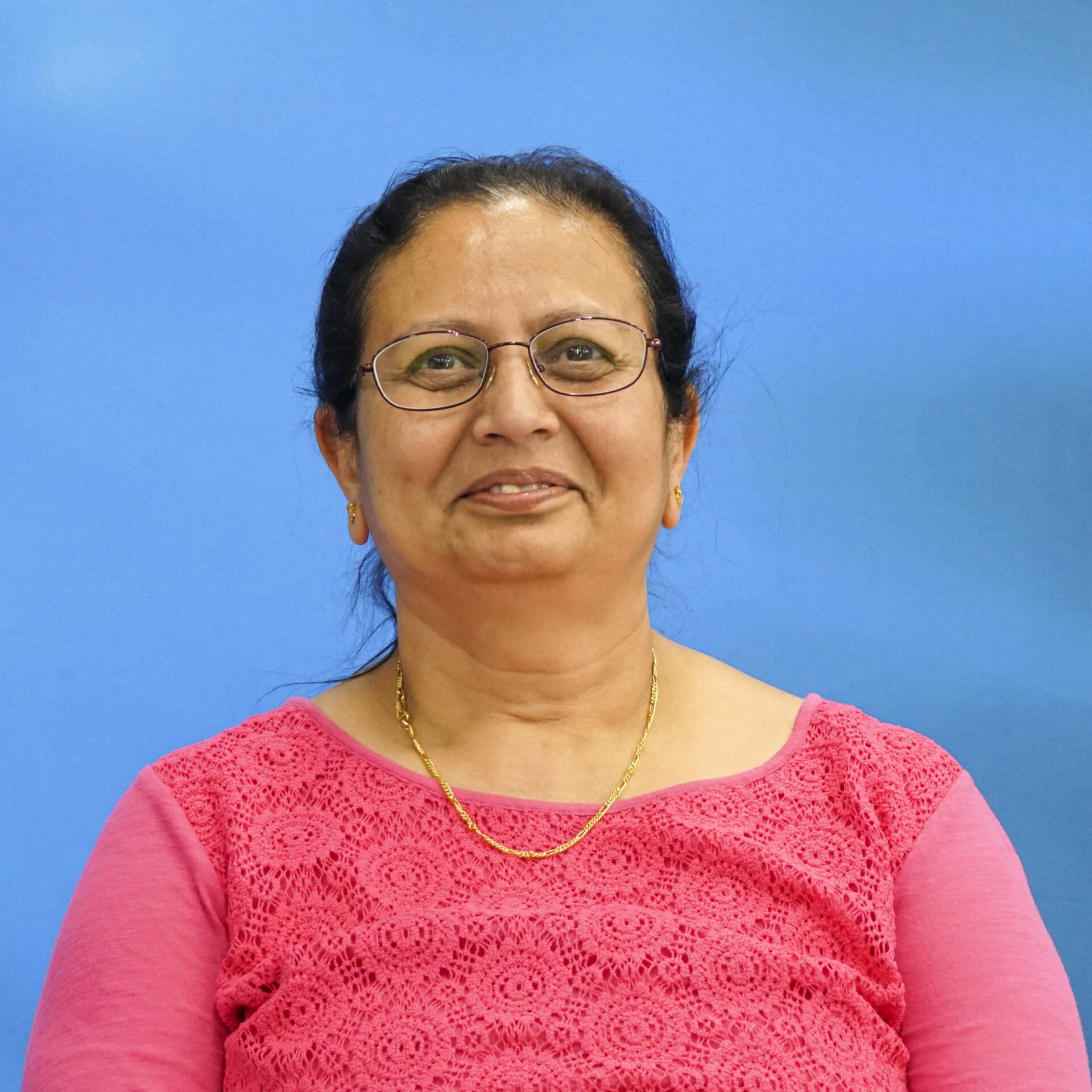 A woman in pink shirt and gold necklace.