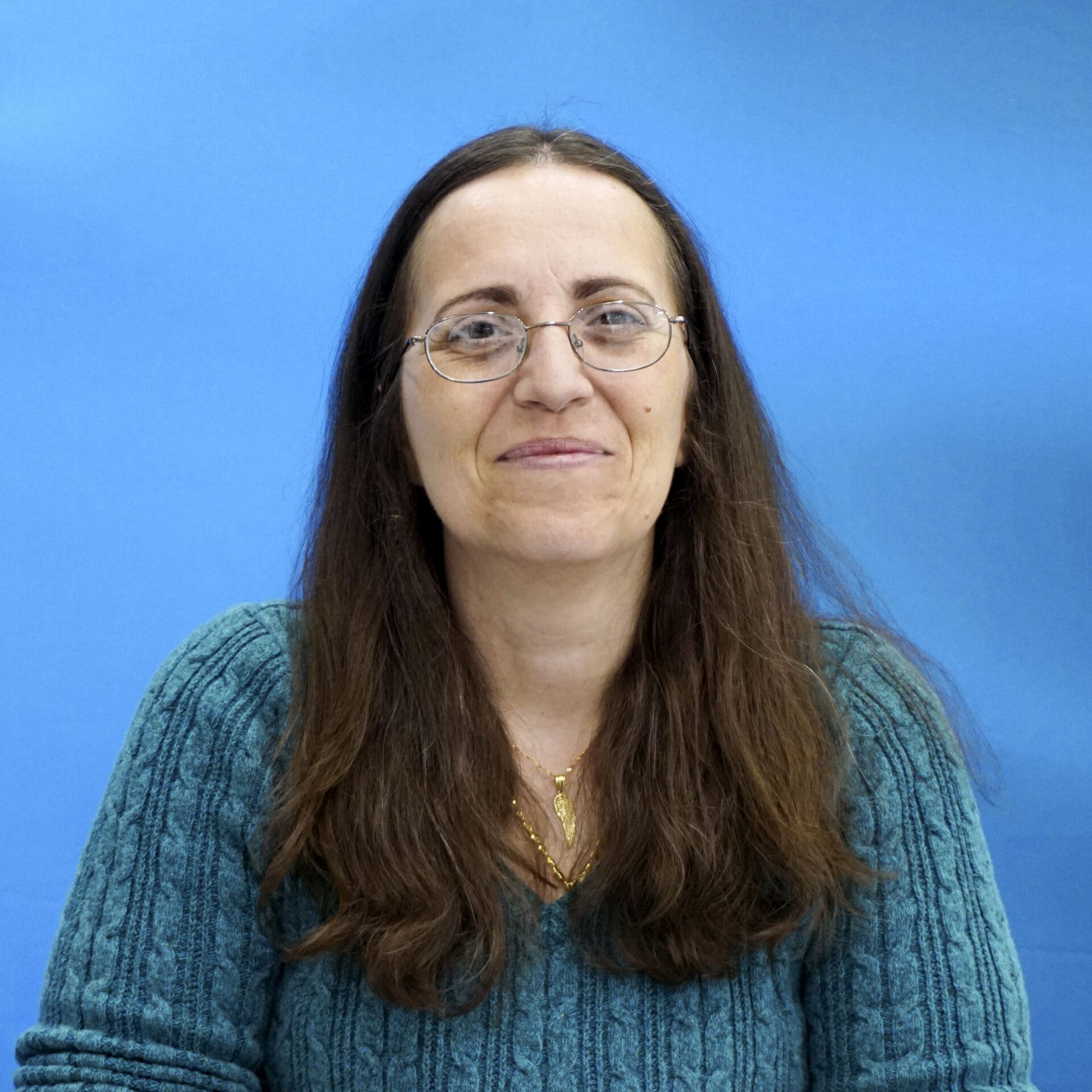 A woman with long hair and glasses is smiling.