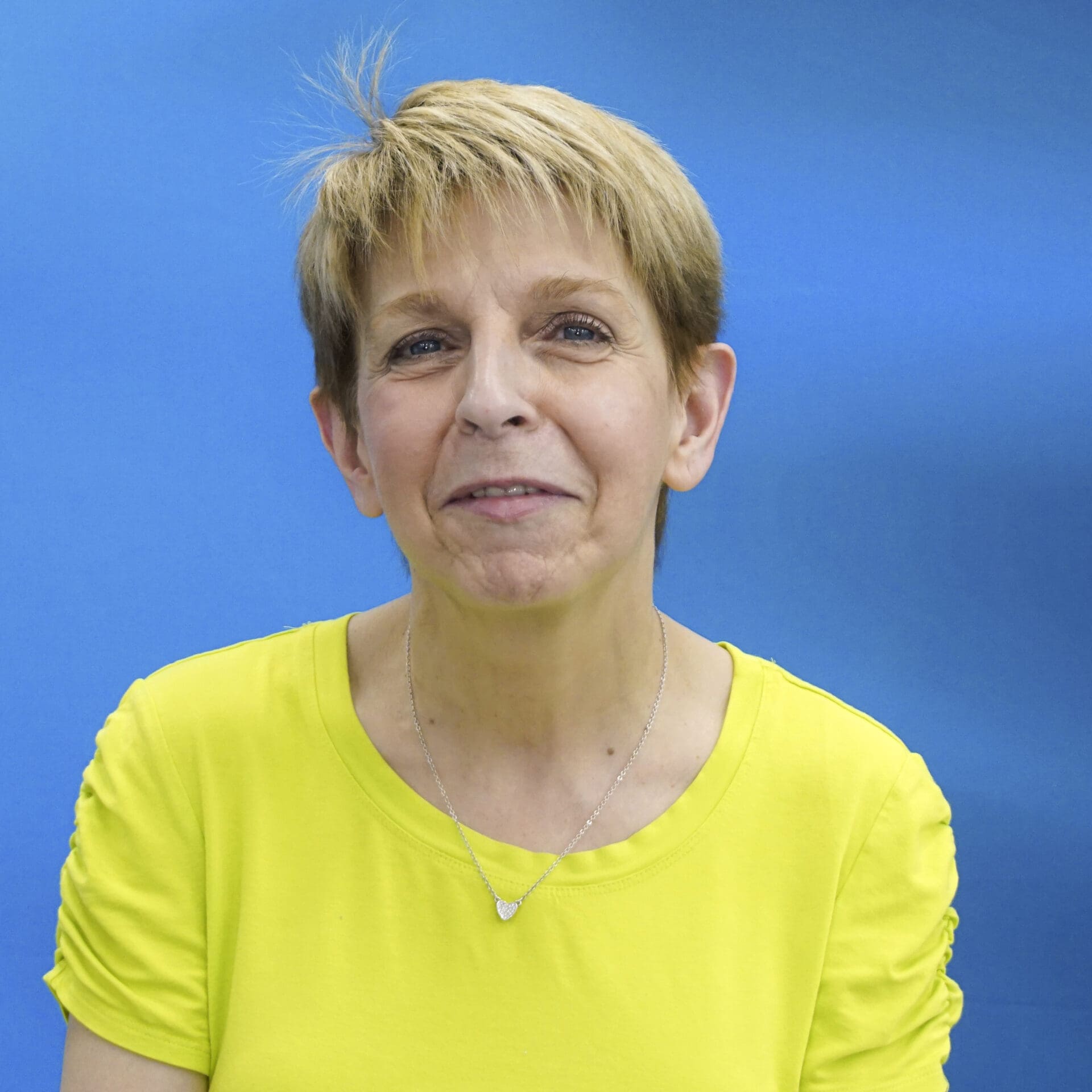 A woman in yellow shirt standing next to blue wall.