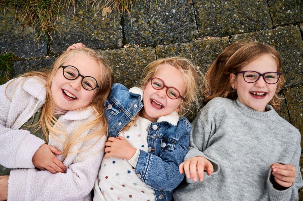 Three young girls are smiling while laying on the ground.