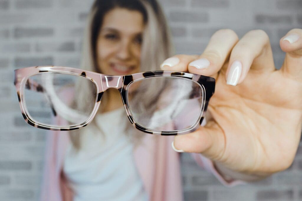 A woman holding up her glasses to the camera.